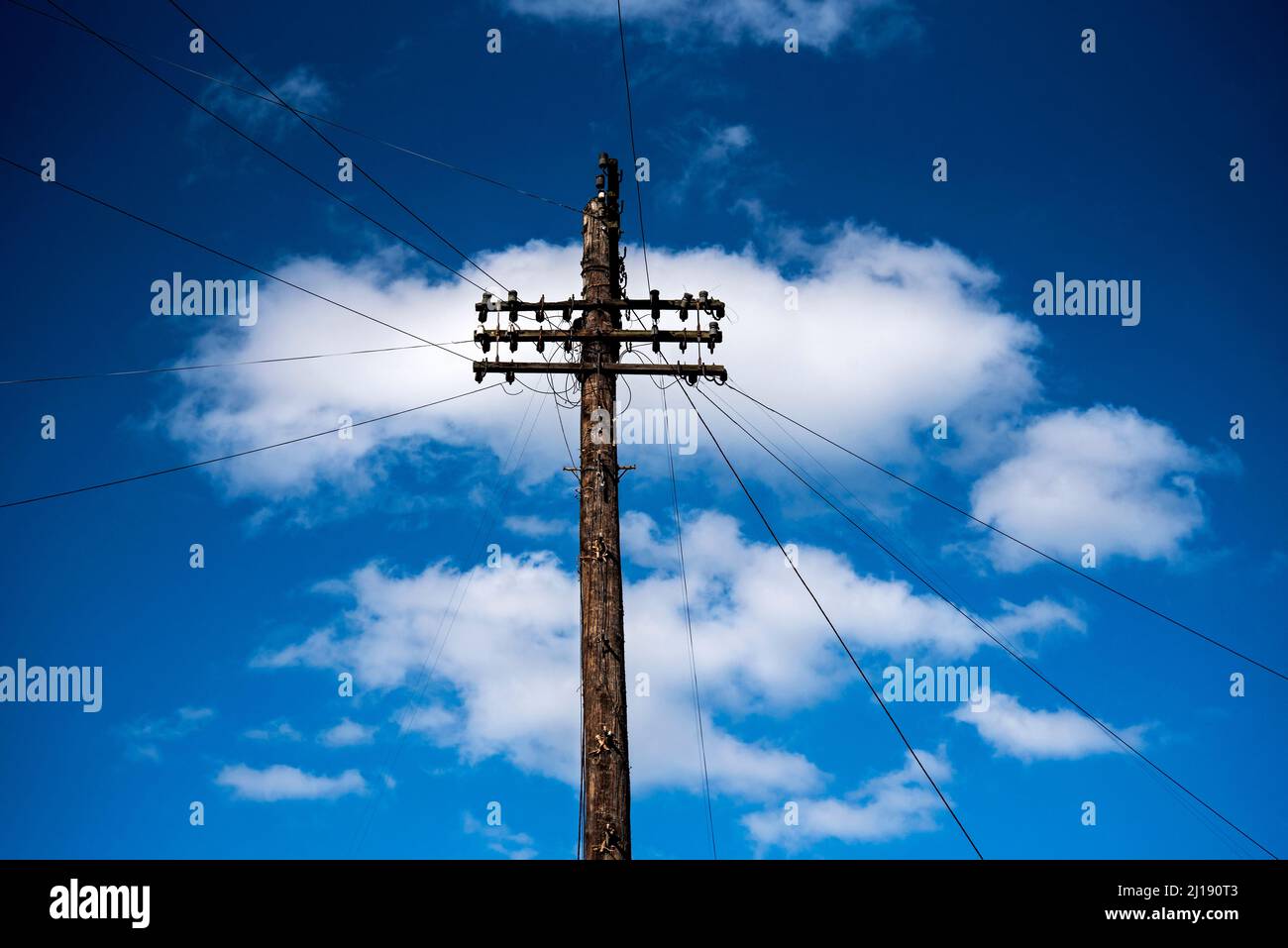 Palo Telegraph contro un cielo blu con nuvole bianche, fili telefonici che vanno via in tutte le direzioni. Foto Stock