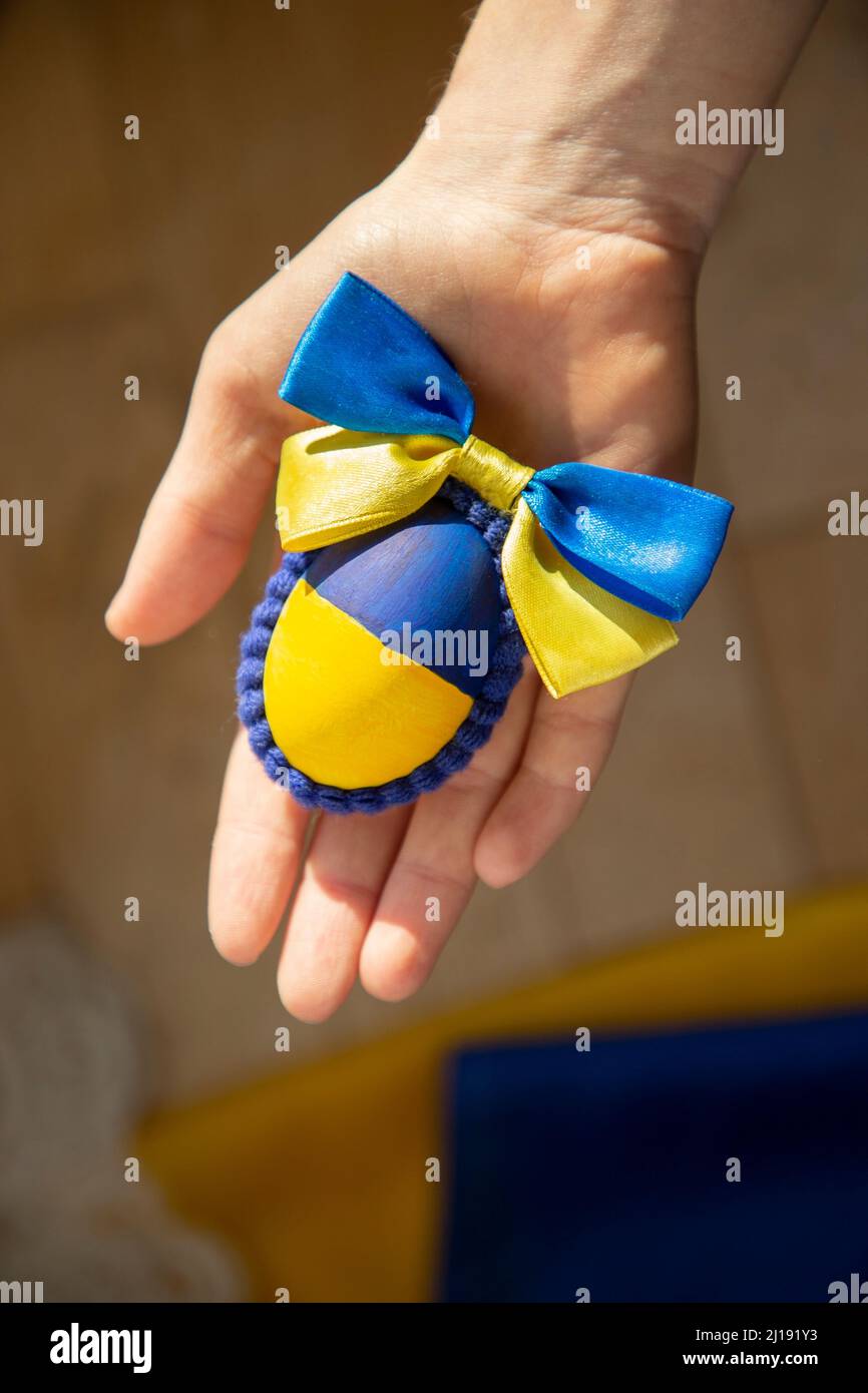 La mano della donna tiene un uovo di pollo pasquale dipinto nei colori giallo-blu della bandiera Ucraina. Vacanza al sole. Il concetto di Pasqua supporta l'Ucraina Foto Stock