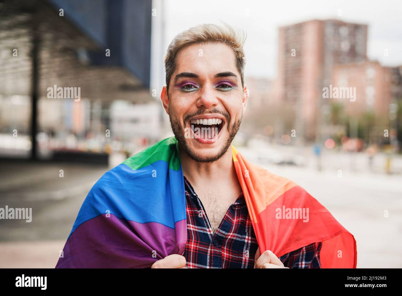 Gay uomo con trucco per divertirsi indossando la bandiera arcobaleno lgbt outdoor - Focus on Face Foto Stock