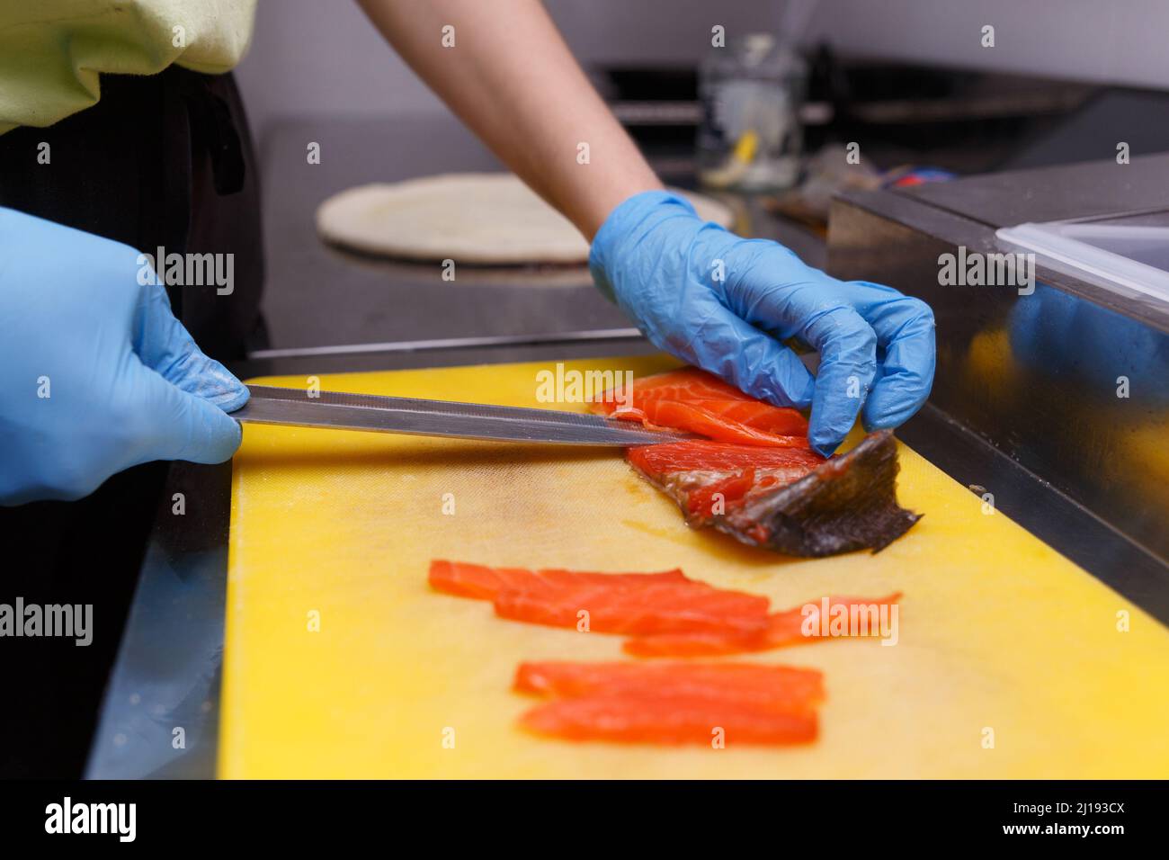 Le mani del cuoco in guanti igienici con un coltello affilato separano i filetti di salmone dalle ossa. Taglio di pesce fresco in cucina su un taglio Foto Stock