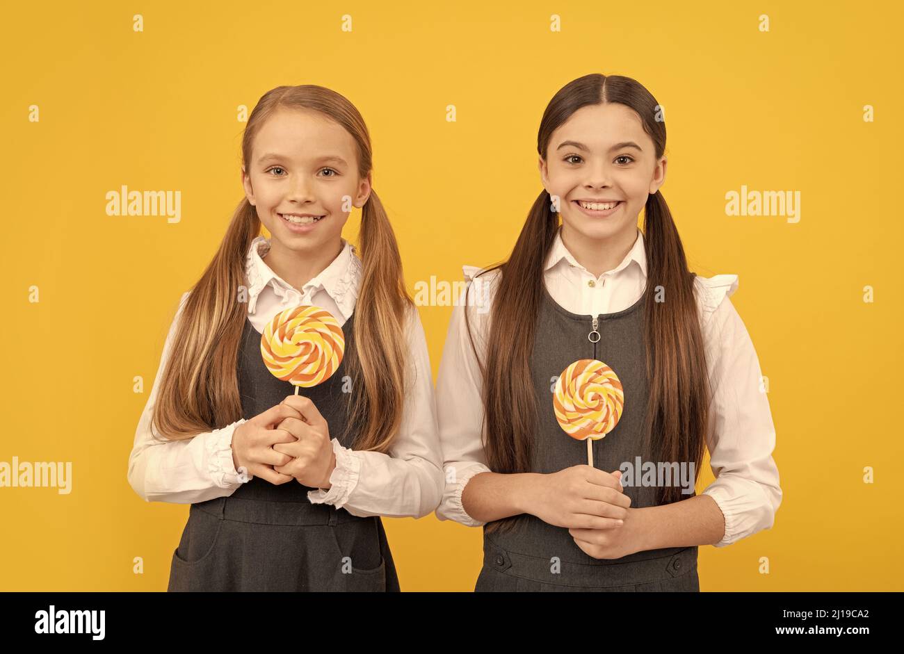 I bambini felici nelle uniformi della scuola tengono i lollipops lo sfondo giallo, i denti dolci Foto Stock