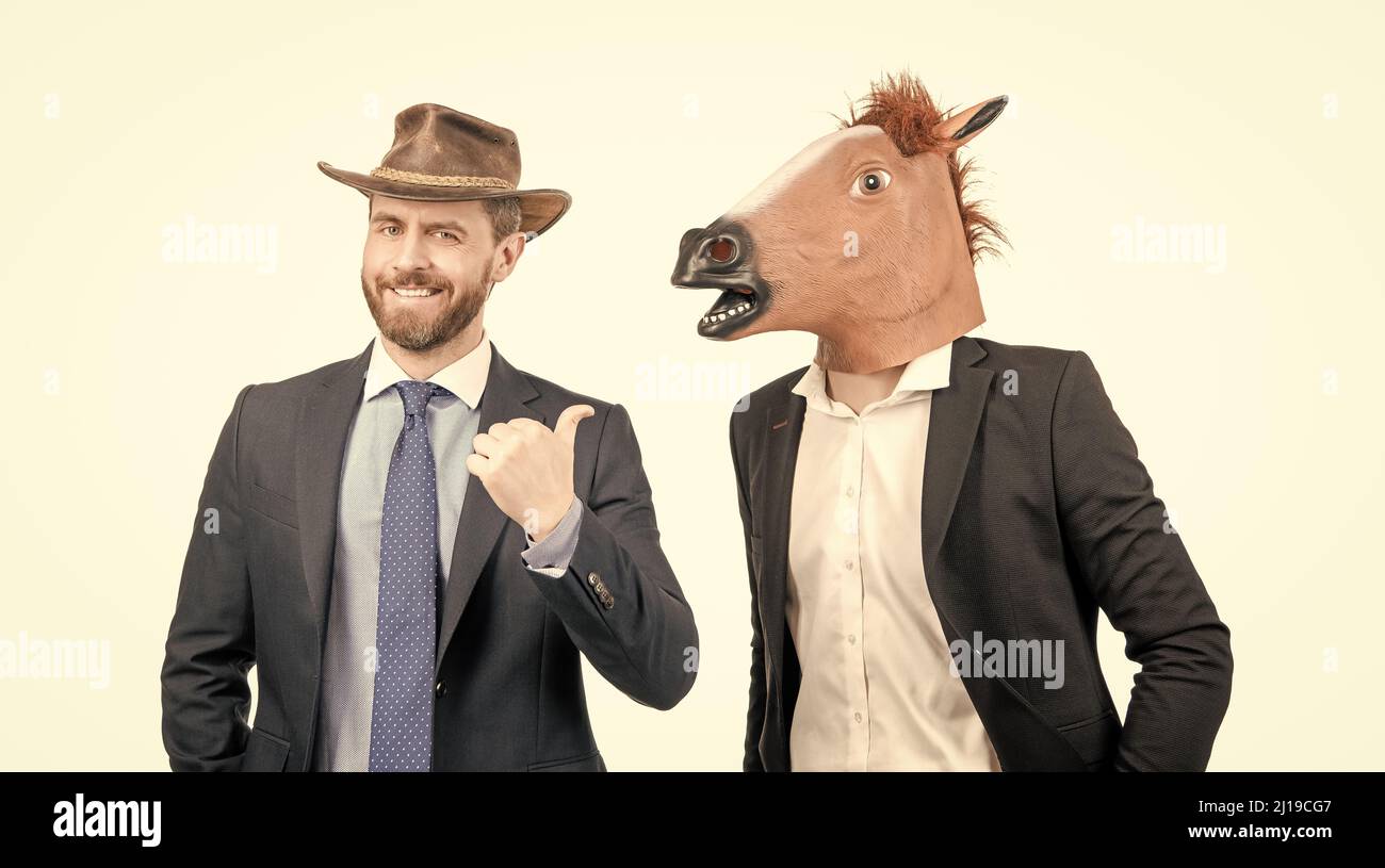 L'uomo di cowboy felice punta il dito contro l'uomo d'affari che indossa la testa del cavallo. Festa occidentale. Cowboy party Foto Stock