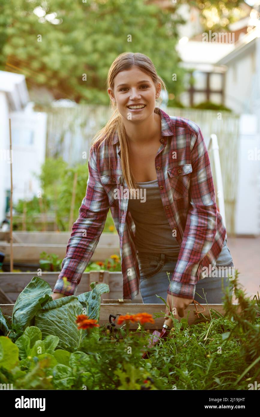 Crescere il tipo di vita che si desidera. Scatto di una bella giovane donna affollata con le sue piante nel suo giardino di casa. Foto Stock