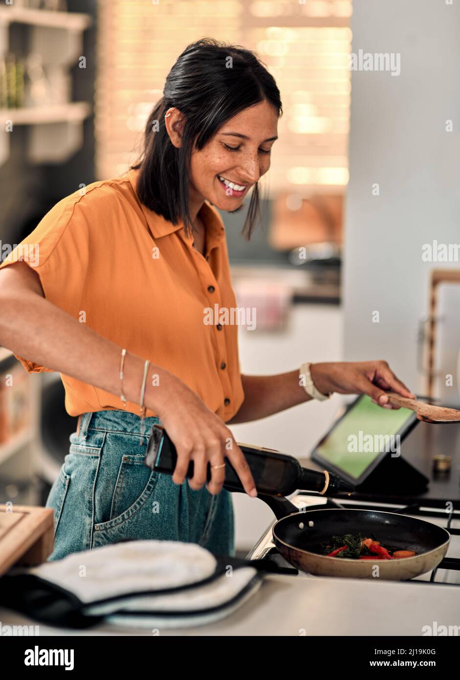 Olio d'oliva, il buon tipo di grasso. Shot di una giovane donna felice che prepara un pasto sano a casa. Foto Stock