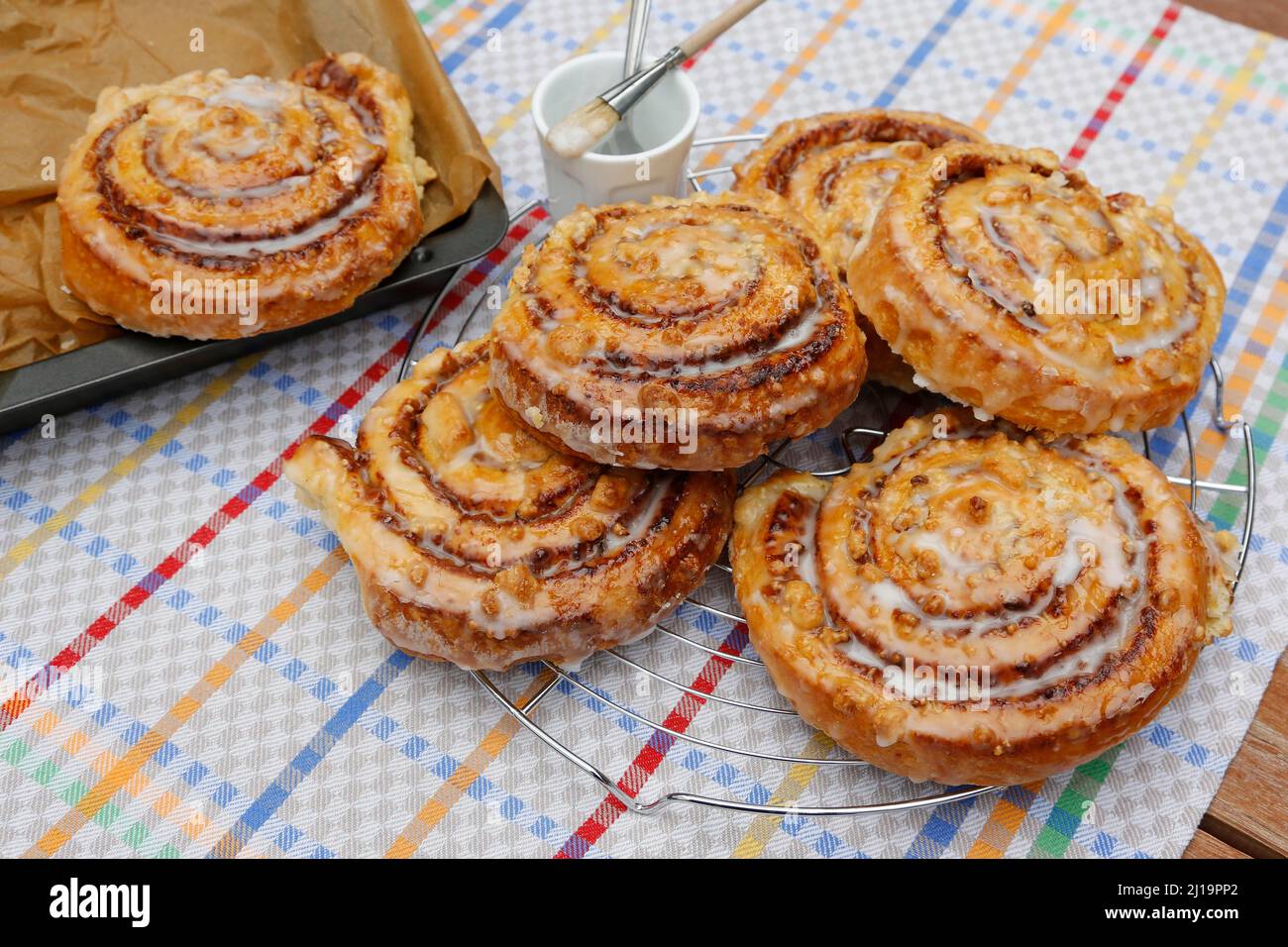 Cucina sveva, cottura, rotolo di cannella su griglia di raffreddamento, vassoio da forno, pennello per spennellare con glassa, dolce lievito di pasticceria con noci, briciole e glassa Foto Stock