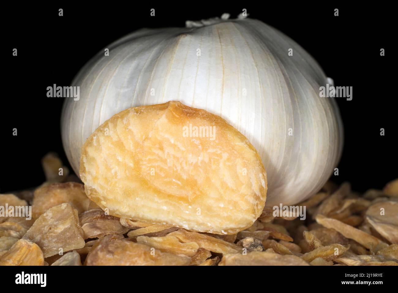 Bulbo di aglio fresco adagiato su fette di aglio essiccato, fotografia da studio con sfondo nero Foto Stock