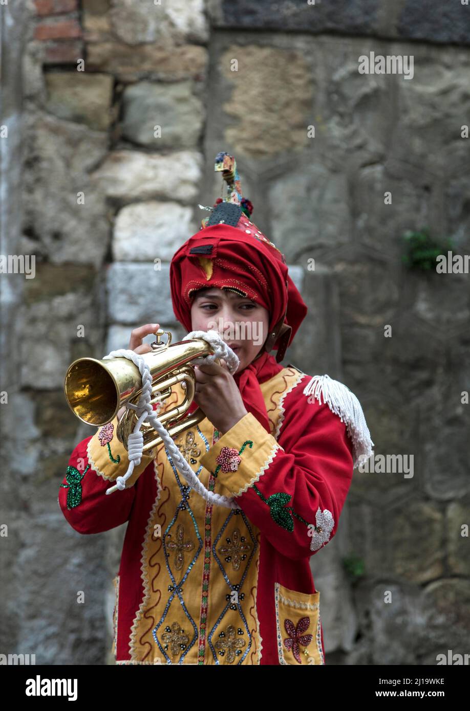 Un giovane vestito come uno dei Judei con il cappuccio rivolto verso l'alto, suonando la tromba durante il Venerdì Santo in una delle antiche strade di San Fratello, provincia di Foto Stock