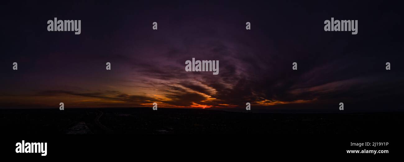 Nuvole scure e spionde in un profondo cielo viola nel bagliore di un tramonto arancione panoramica aerea Foto Stock