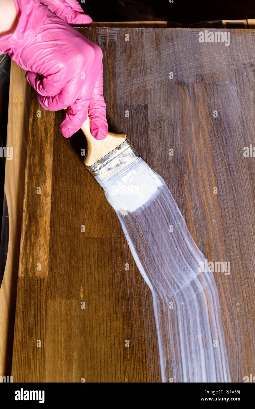 la mano gloved vernicie un asse macchiato della mobilia del pino in casa Foto Stock