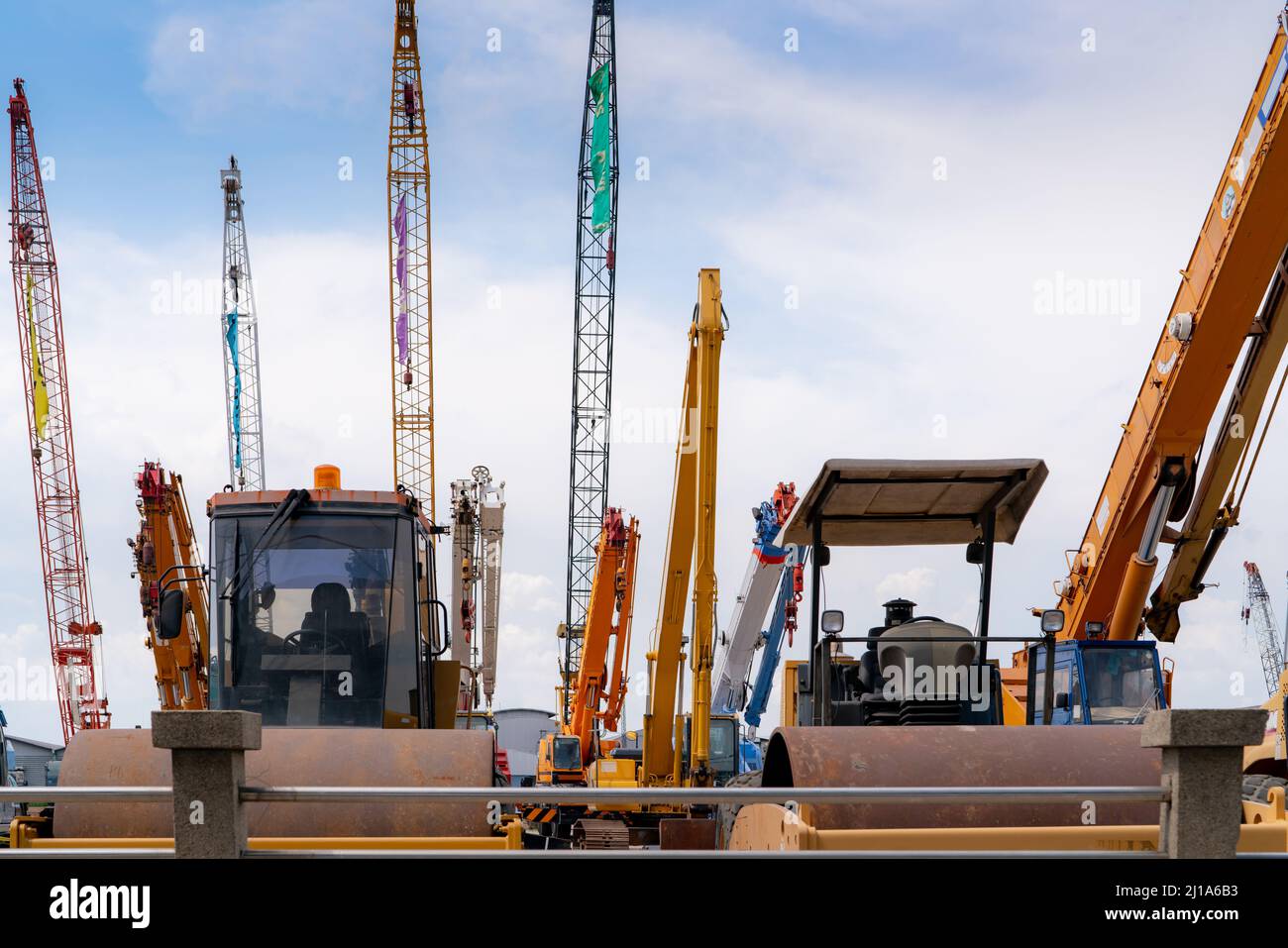 Rullo da strada, gru mobile e retroescavatore con braccio lungo. Macchinari pesanti parcheggiati in un cantiere d'asta per macchinari di seconda mano. Rullo da strada, gru mobile. Foto Stock