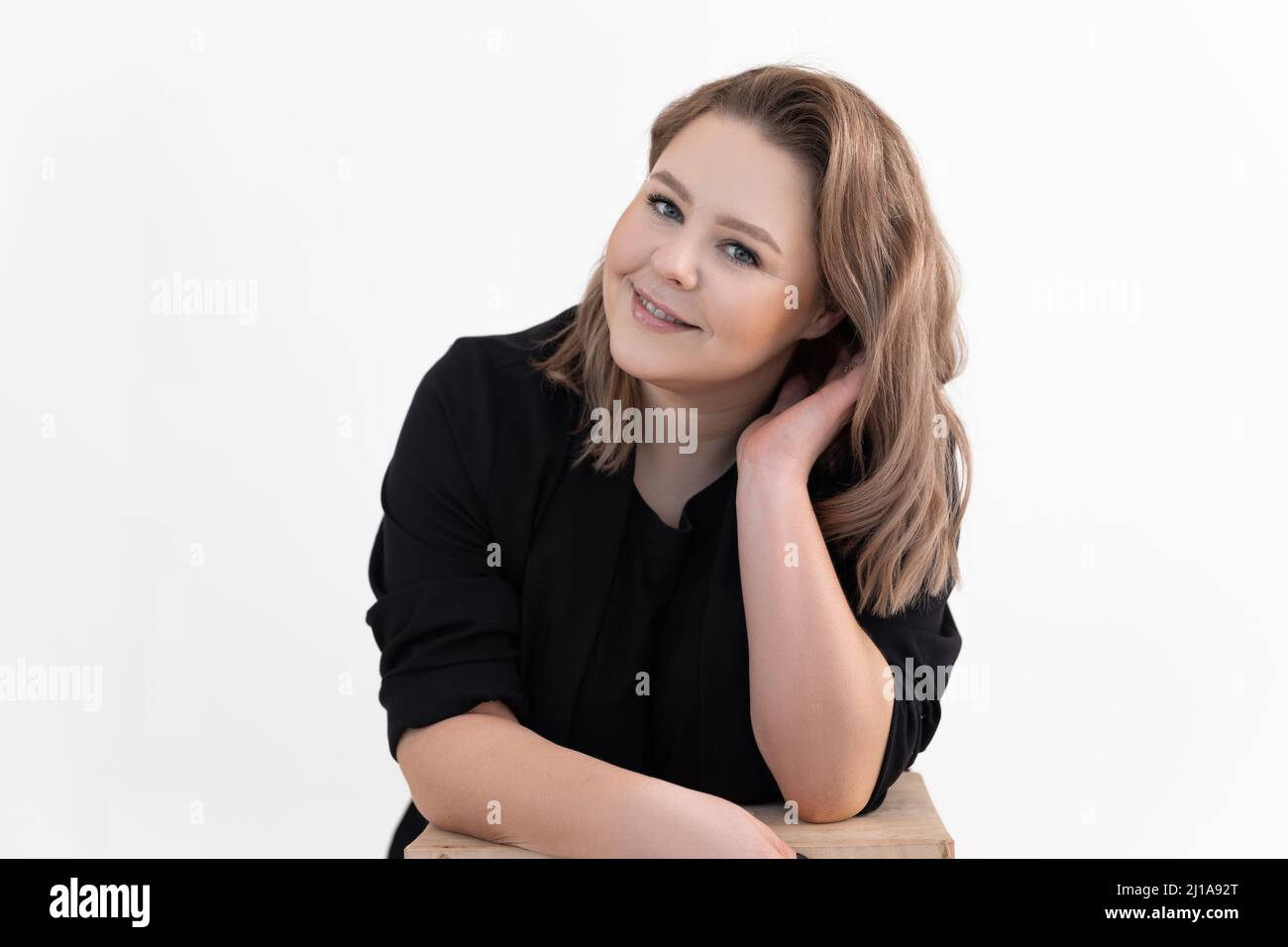 Ritratto di sorridente mezza età grasso sovrappeso donna titivating lunghi capelli scuri indossando cardigan nero, seduto a tavola. Foto Stock
