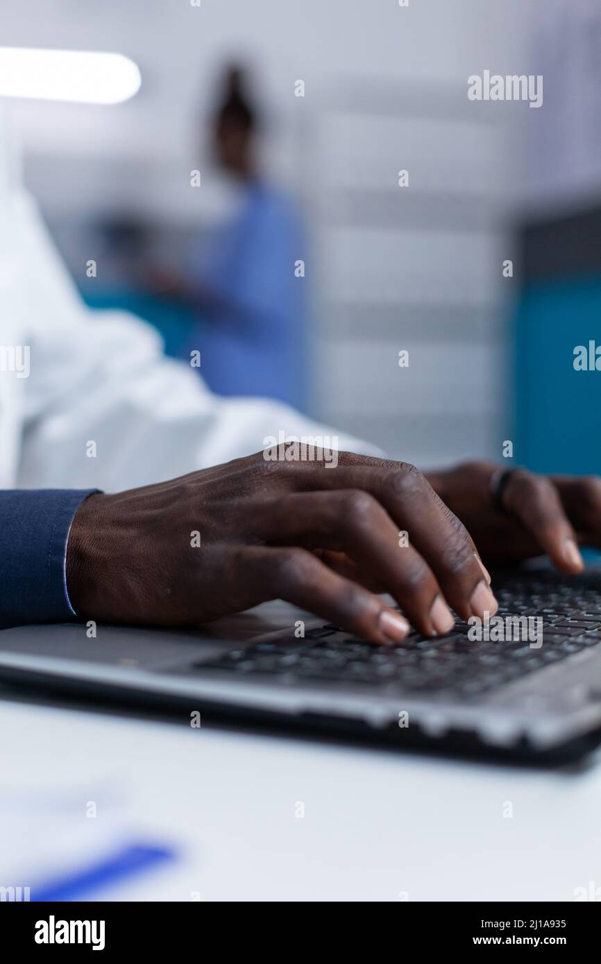 Primo piano del medico ospedaliero utilizzando il computer portatile per controllare la cartella dei pazienti e il programma di trattamento. Specialista medico clinico che controlla il database dei medicinali prescritti mentre segnala le condizioni del paziente Foto Stock