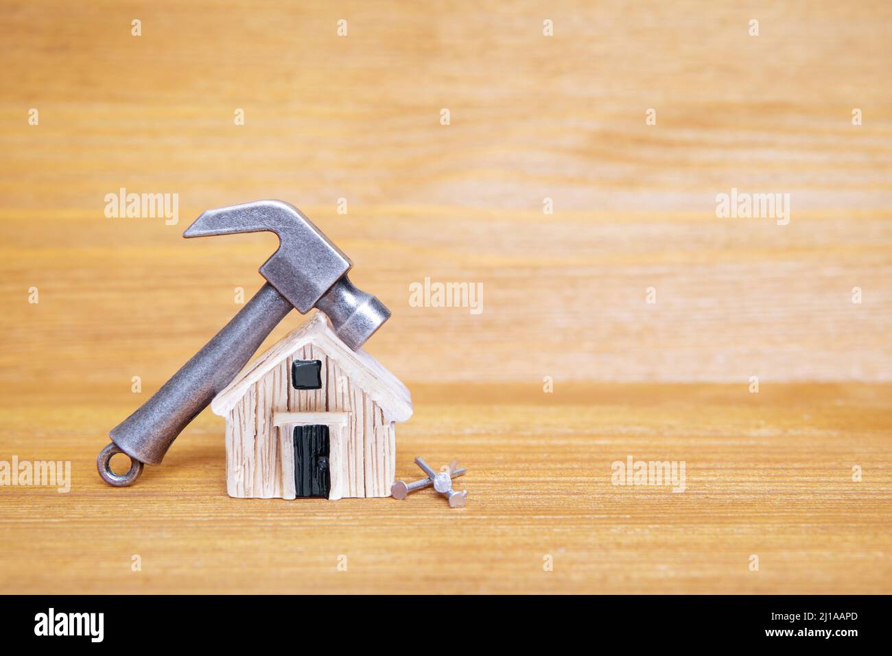 Piccolo martello e chiodi in acciaio da una casa giocattolo in miniatura su uno sfondo di legno. Concetto di ristrutturazione della casa. Foto Stock