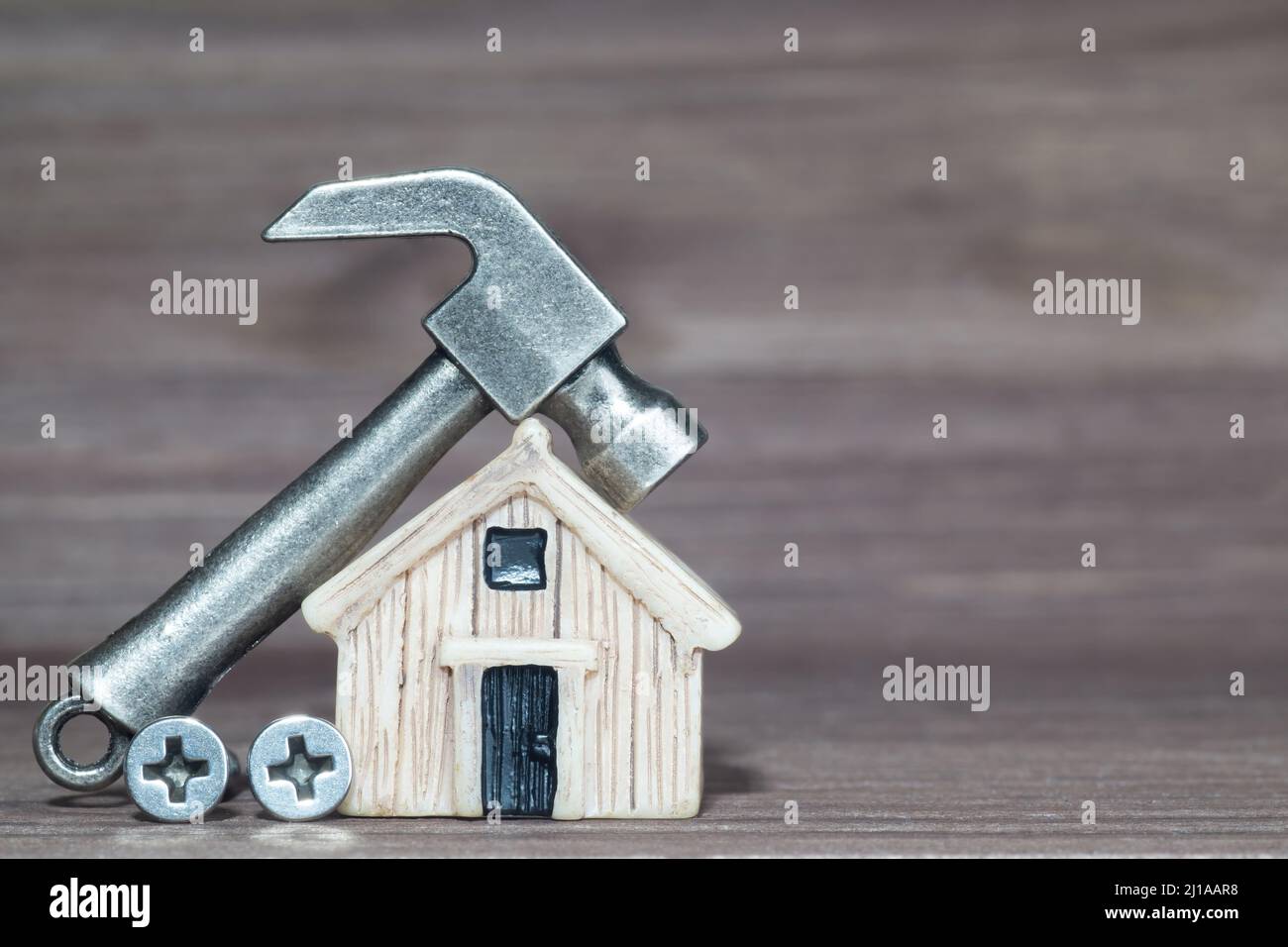 Piccolo martello in acciaio e viti da un modello di casa in miniatura su uno sfondo in legno. Concetto di riparazione domestica. Foto Stock