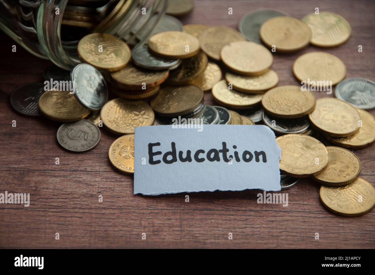 Testo didattico su carta strappata con vasetto, monete e sfondo in legno da tavola. Concetto di istruzione e risparmio Foto Stock