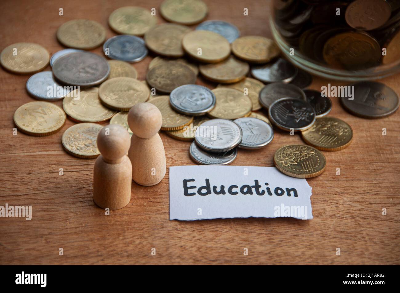 Testo didattico su carta strappata con vasetto, monete, bambole in legno e sfondo tavola in legno. Concetto di istruzione e risparmio Foto Stock