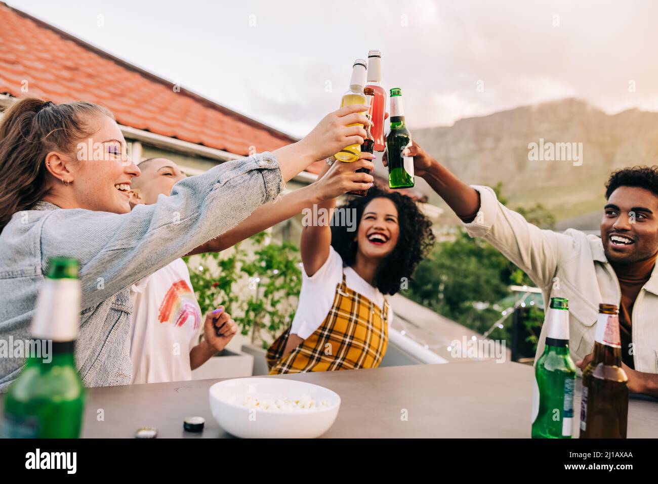 Grazie per il fine settimana. Gruppo di giovani amici felici che fanno un brindisi con birre fredde mentre si aggrappano insieme su un tetto. Allegri giovani amici lau Foto Stock