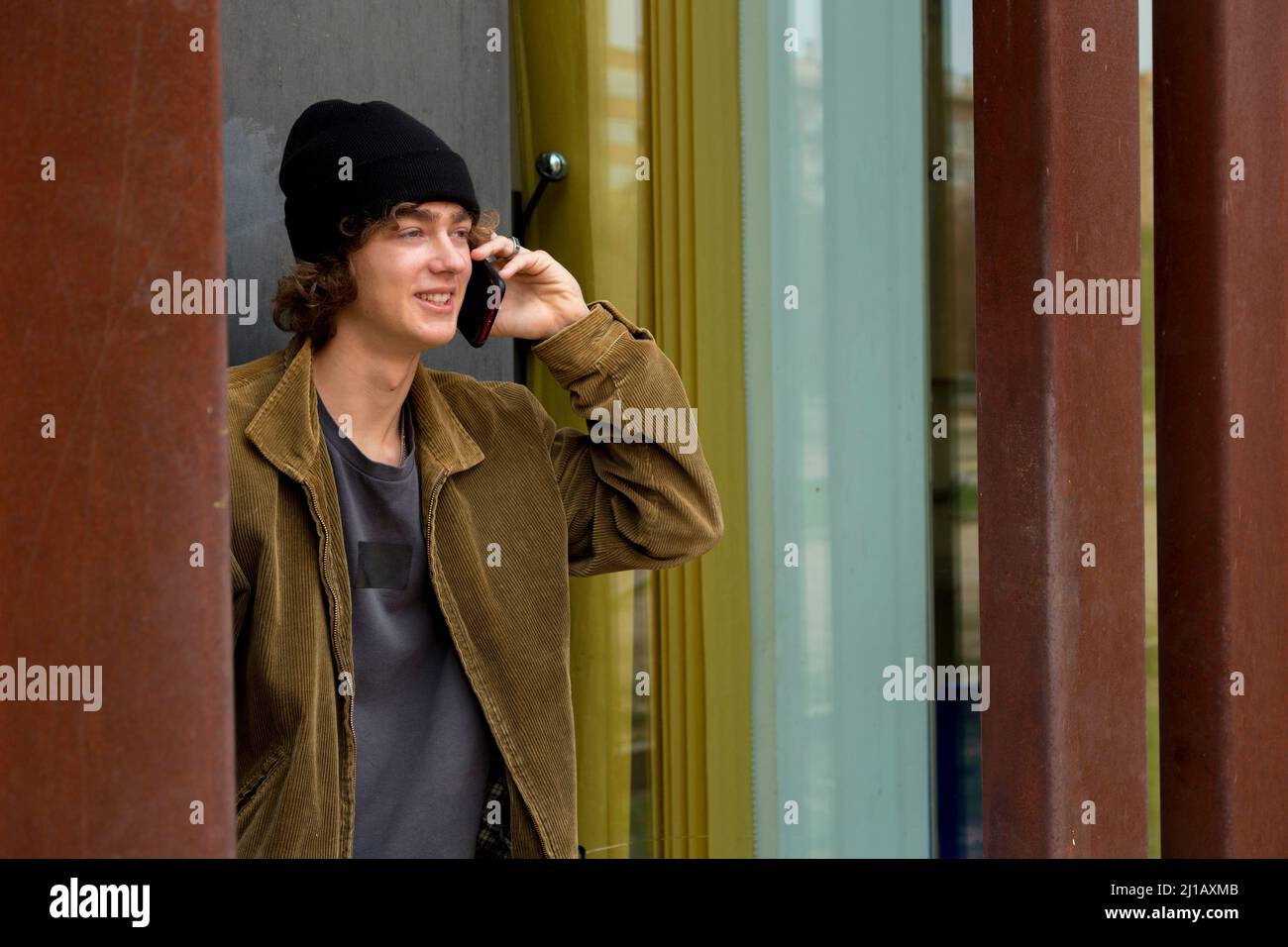 adolescente studente universitario in cap parlare sul cellulare avendo un buon tempo e sorridendo Foto Stock