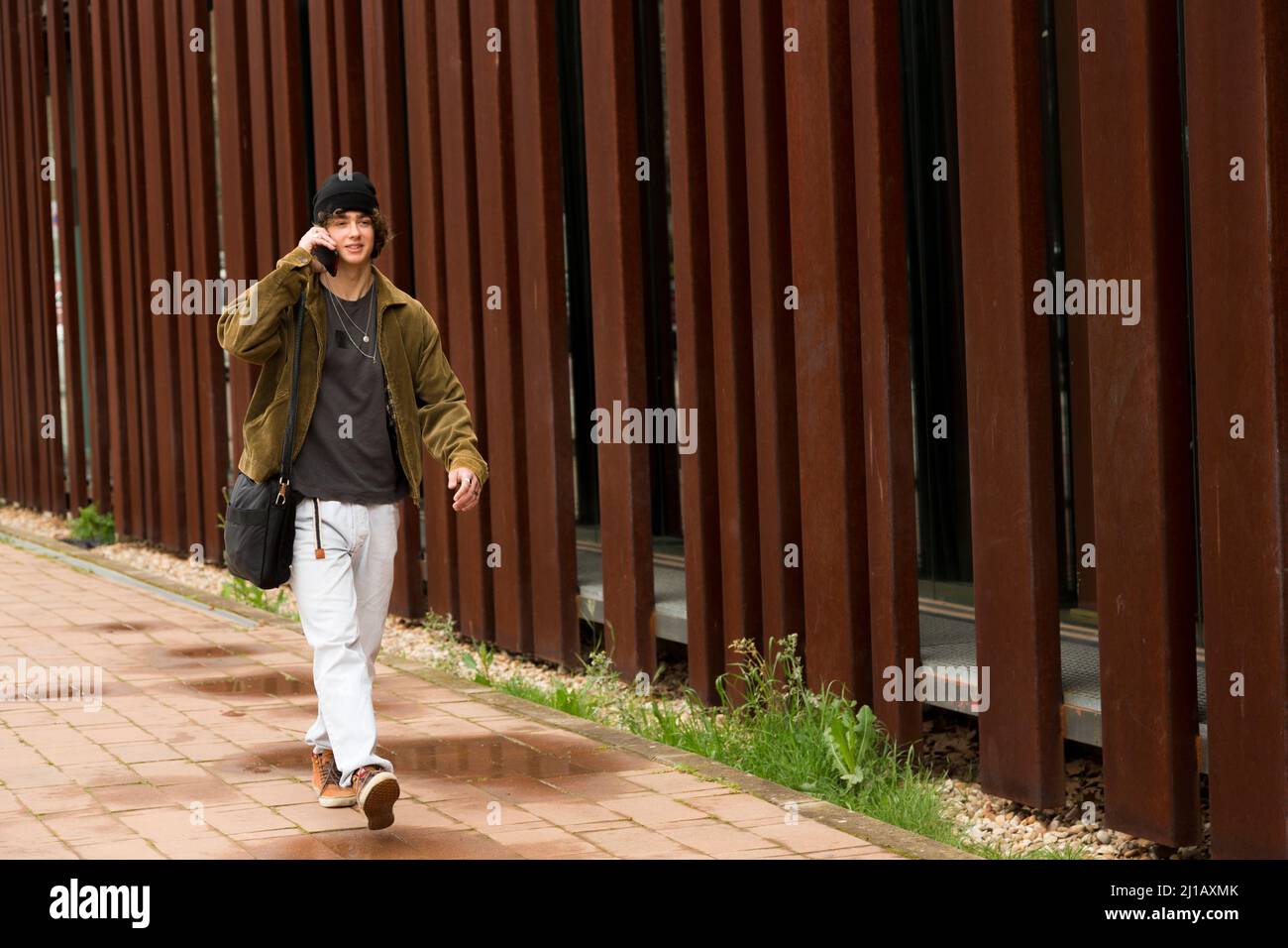 giovane studente universitario vestito di abbigliamento casual parlando su un telefono cellulare a piedi per la strada in autunno Foto Stock