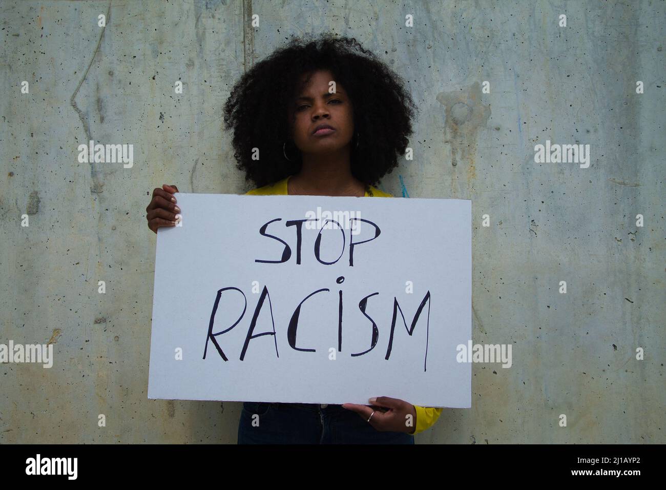 Una donna afroamericana sostiene una bandiera che legge STOP RAZZISMO. Nella parete grigia di sfondo. Foto Stock
