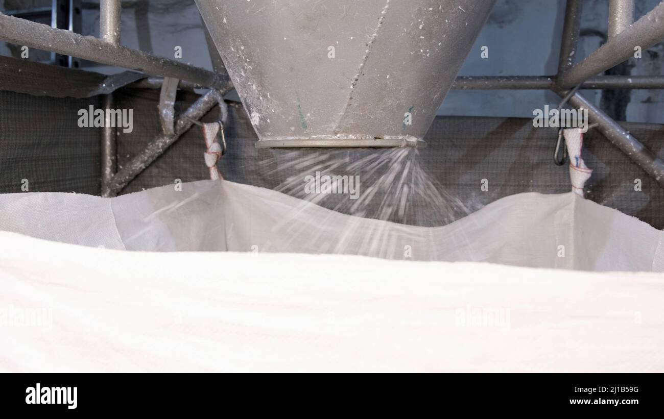 Dal ciclone della macchina esce plastica dura macinata bianca mediante trasporto pneumatico nel sacco grande. Concetto di materiali riciclabili, plastica Foto Stock