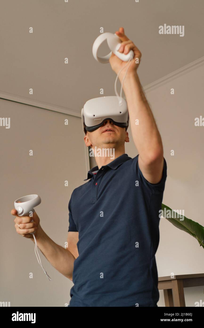 Il giovane uomo in abiti casual gioca giochi virtuali a casa. Il casco VR uomo in realtà virtuale compensa la mancanza di movimento. Foto Stock
