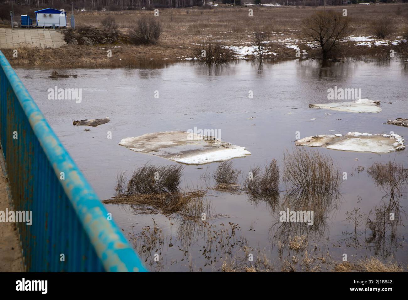 Il ghiaccio sporco galleggia lentamente lungo il fiume. Primavera, neve si scioglie, erba secca tutto intorno, le inondazioni iniziano e il fiume trabocca. Giorno, tempo nuvoloso, luce calda e soffusa. Foto Stock