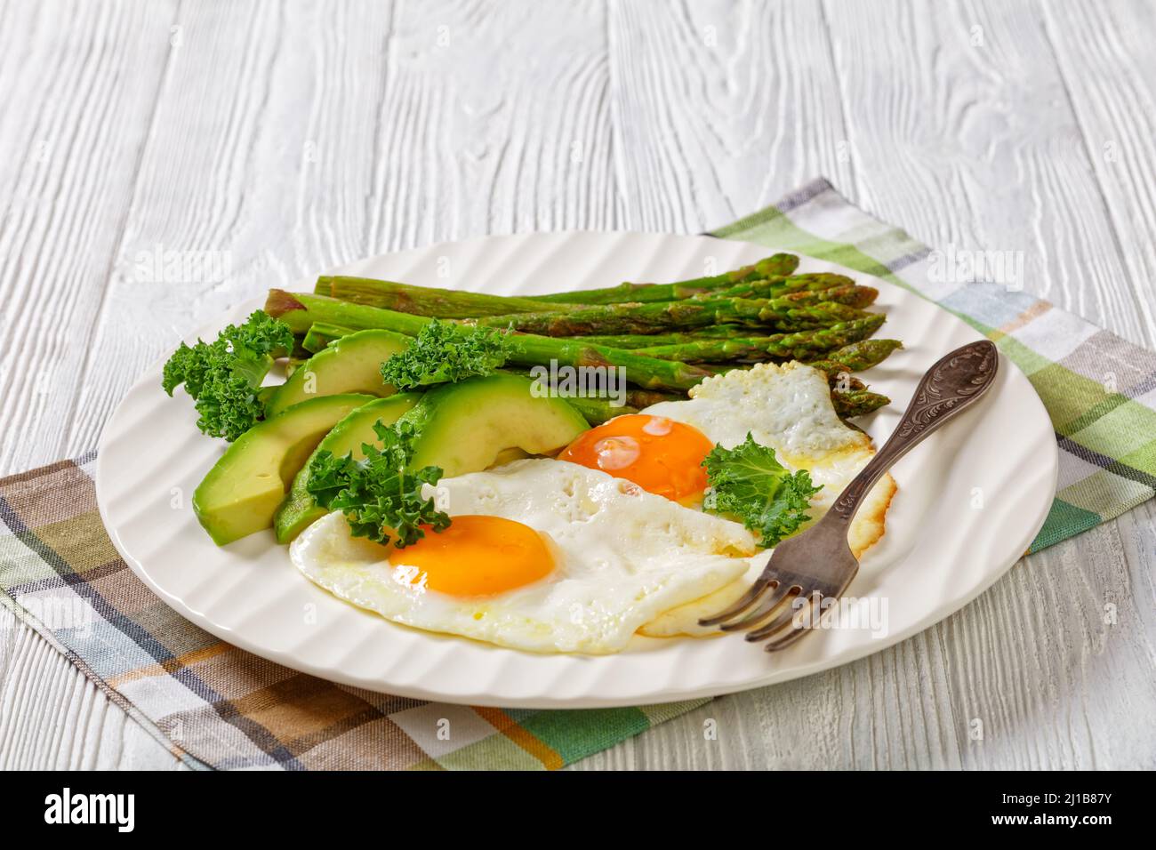 asparagi cotti, avocado fresco maturo e uova fritte con tuorli runny su un piatto bianco, vista orizzontale, primo piano, spazio libero Foto Stock