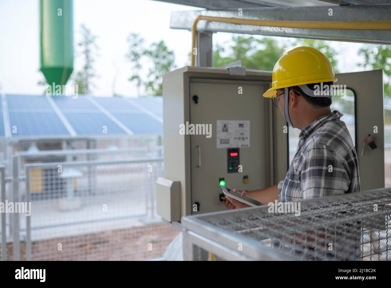 Il tecnico di una stazione di pompaggio delle acque sotterranee con energia solare o alternativa utilizza un tablet per il controllo e il monitoraggio. Foto Stock