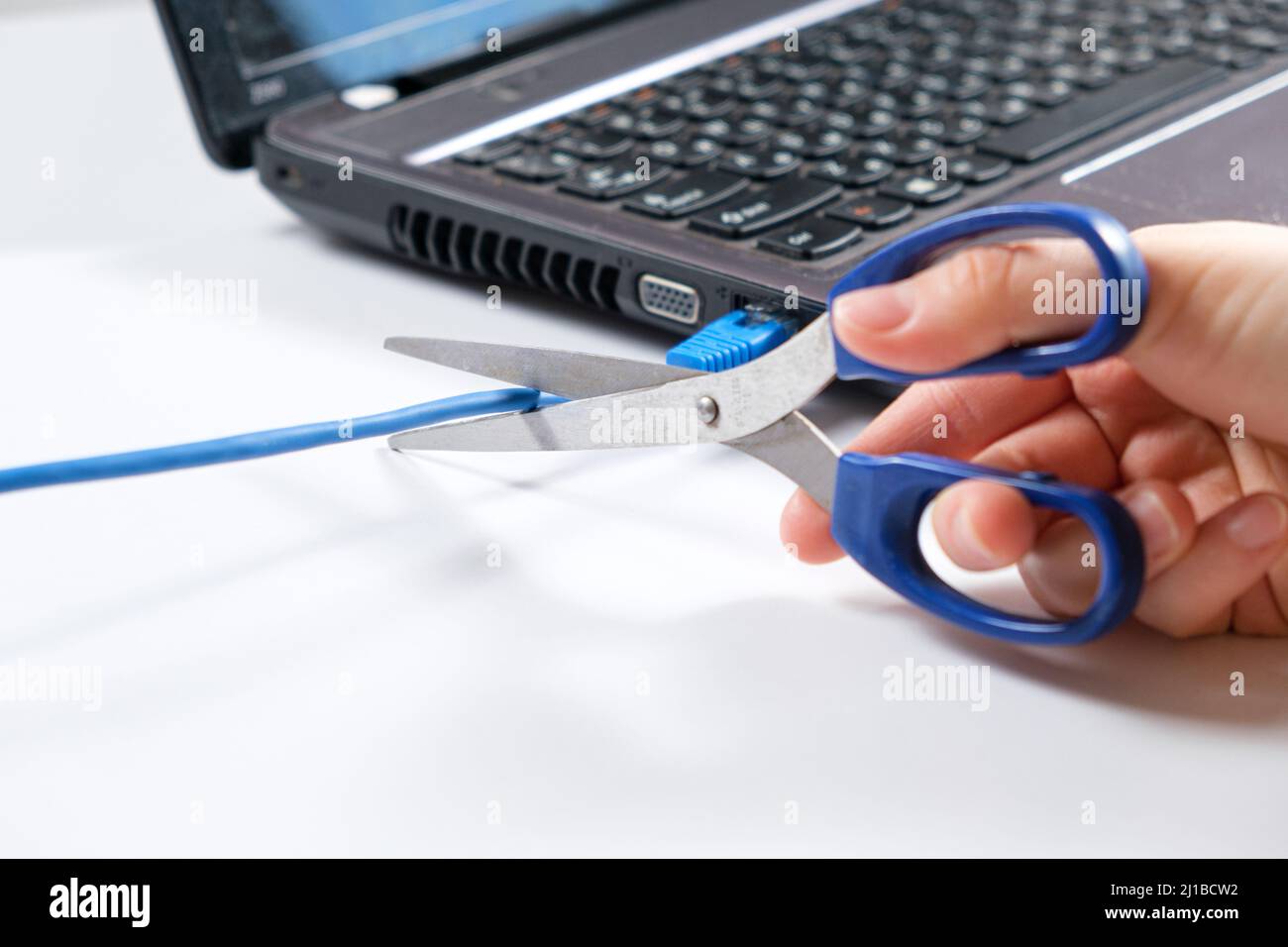 Le forbici tagliano il cavo Internet collegato al computer portatile. Spegnimento di Internet, wi-fi Foto Stock