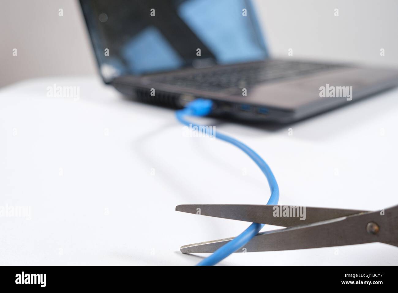 Le forbici tagliano il cavo Internet collegato al computer portatile. Spegnimento di Internet, wi-fi Foto Stock