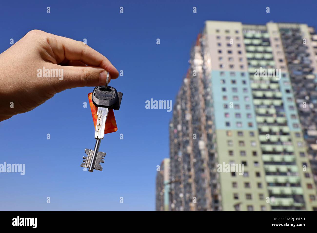 Le chiavi della casa in mano maschile sullo sfondo del nuovo edificio della torre. Agente immobiliare, casa in movimento o affitto di proprietà Foto Stock