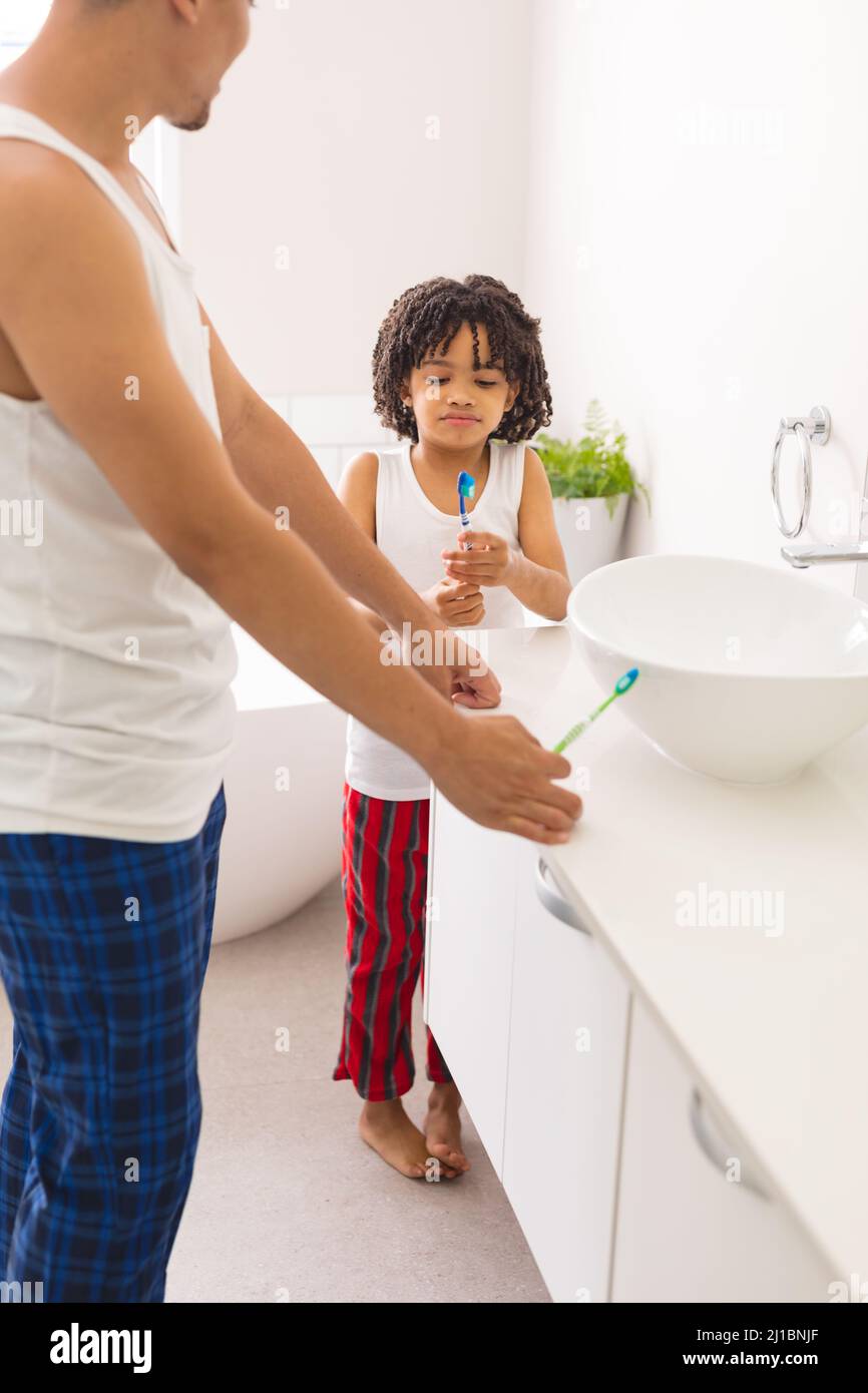 Ragazzo ispanico che guarda il pennello mentre si alza da padre in bagno a casa Foto Stock