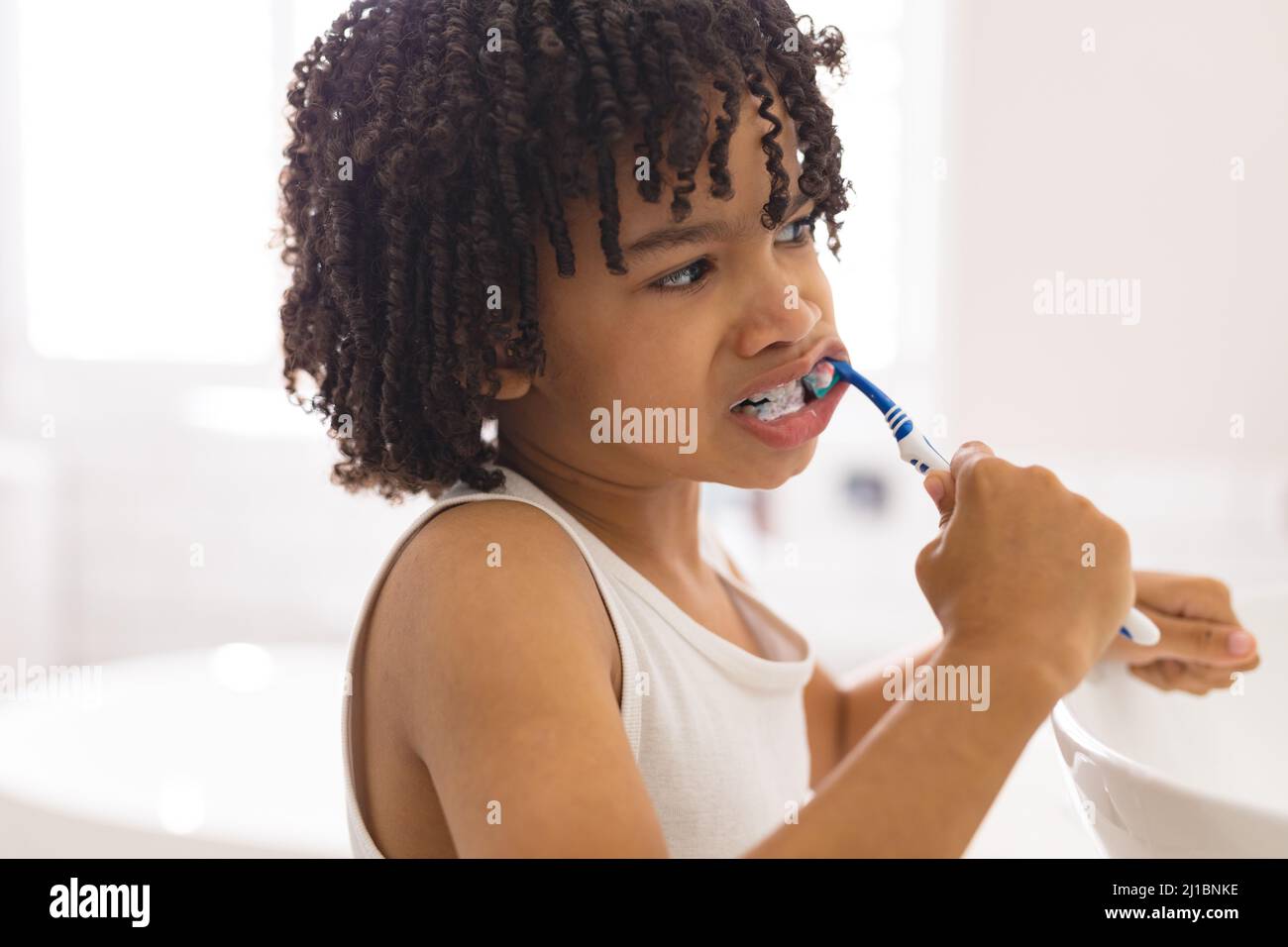 Carino capelli ricci ragazzo ispanico spazzolando i denti in bagno a casa Foto Stock