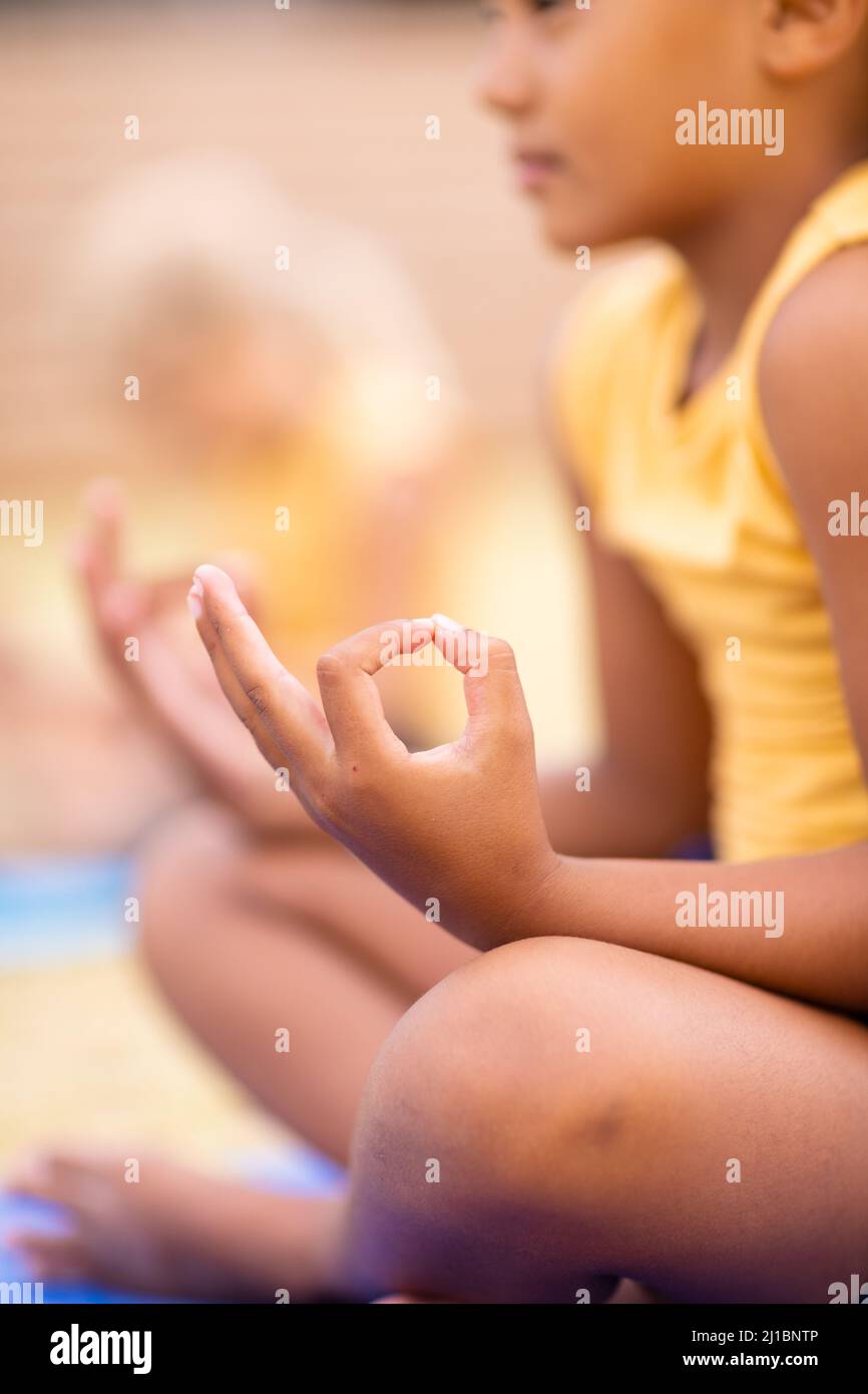 Studentessa biraciale elementare meditando mentre si siede a terra Foto Stock