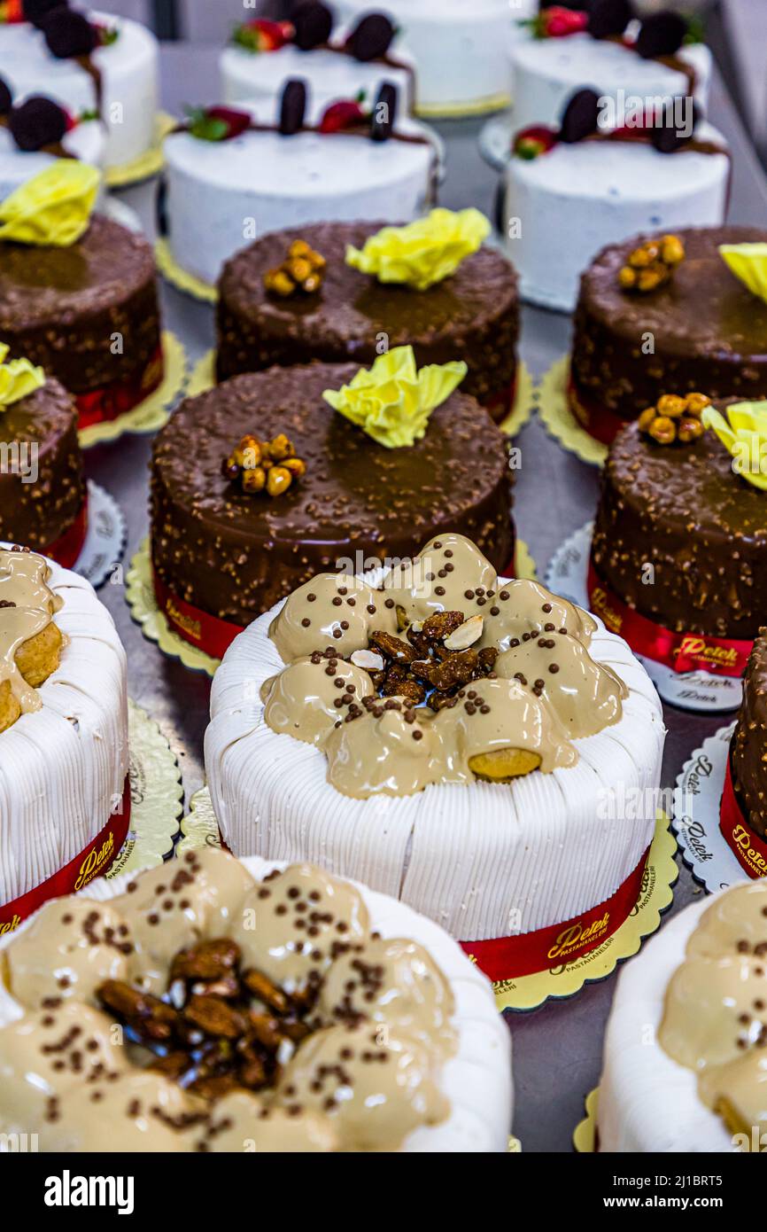 I dolci finiti della pasticceria Petek Pastahanesi sono pronti nella manifattura a Gazimağusa/Famagusta, Repubblica Turca di Cipro del Nord (RTNC): torte alla crema ricoperte di caramello, mandorle tostate e perle di cioccolato in primo piano, torte al cioccolato ricoperte di nocciole con un fiore di cioccolato giallo dietro di loro e torte alla crema bianche con biscotti al cioccolato e fragole più indietro. Il nastro rosso recita "Petek Pastahanesi". La pasticceria è stata fondata nel 1976 da Mehmet Bey e Seher Hanım, è oggi considerata una delle più antiche panetterie di Cipro e dà lavoro a circa 130 persone. Foto Stock
