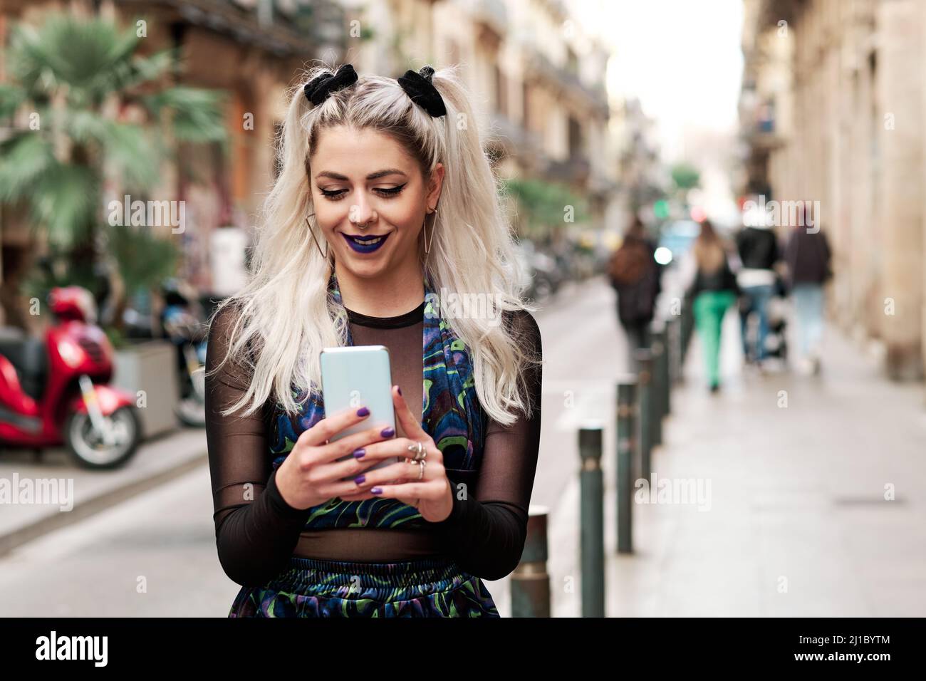 Giovane donna alternativa che usa il suo cellulare mentre cammina lungo la strada. Foto Stock