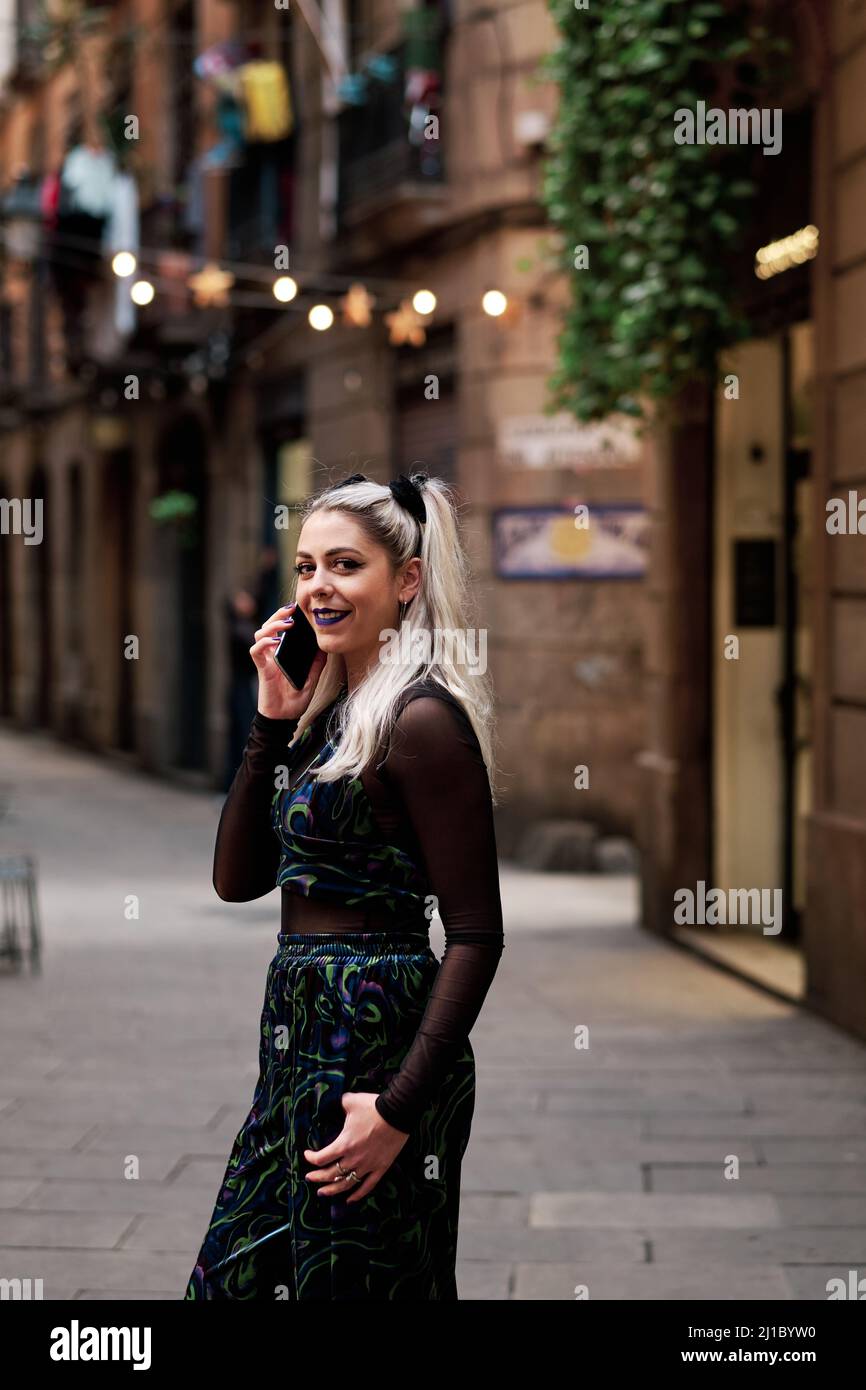 Donna alternativa sorridente mentre parla al telefono all'aperto per strada. Foto Stock