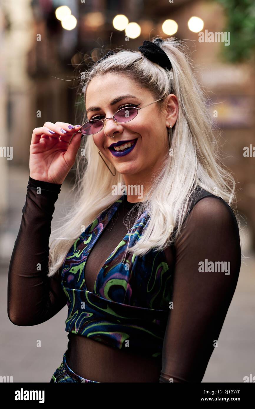 Alternativa giovane donna in occhiali da sole sorridente mentre si posa all'aperto sulla strada della città. Foto Stock