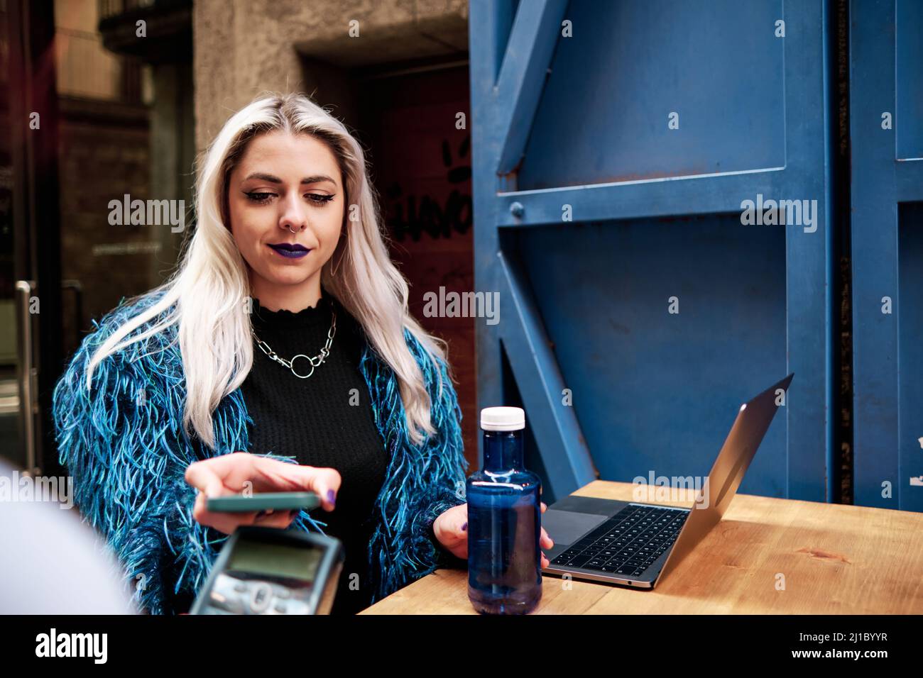 Donna che paga senza contatto con il suo telefono cellulare in un bar. Foto Stock