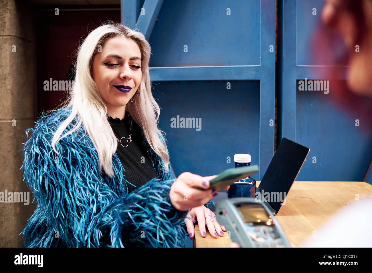 Donna alternativa che paga il conto tramite telefono cellulare utilizzando la tecnologia NFC. Foto Stock