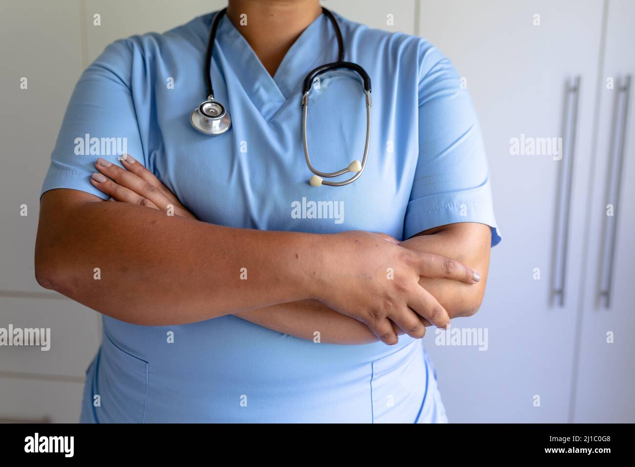 Metà sezione di infermiera femminile afroamericana di metà adulto in piedi con le braccia incrociate e stetoscopio Foto Stock
