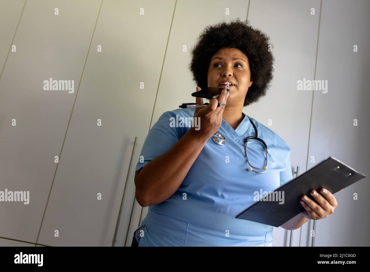 Infermiera di metà adulta afroamericana che parla durante la chiamata mentre tiene gli appunti Foto Stock