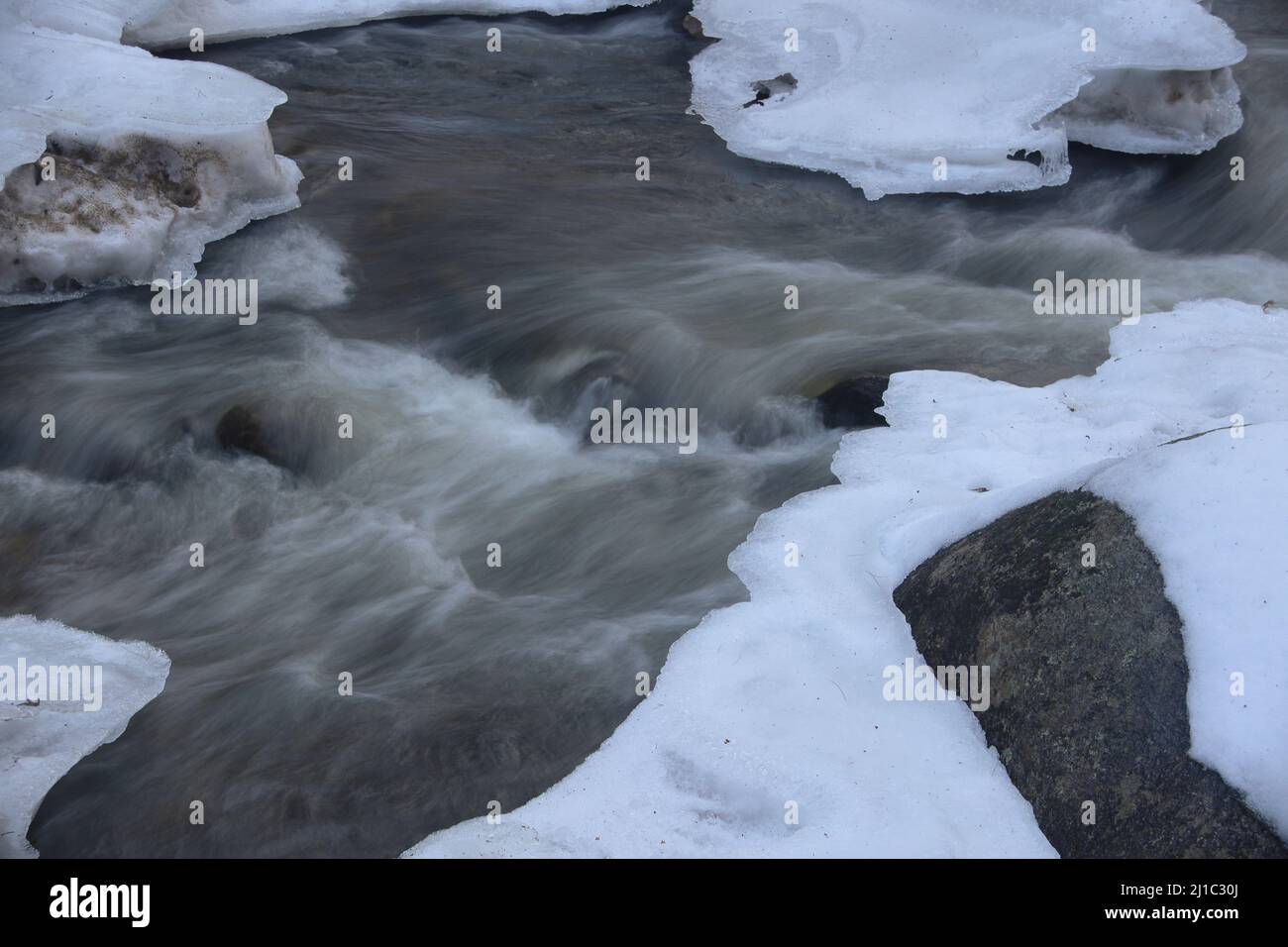 Acqua setosa che scorre su rocce con neve d'inverno Foto Stock