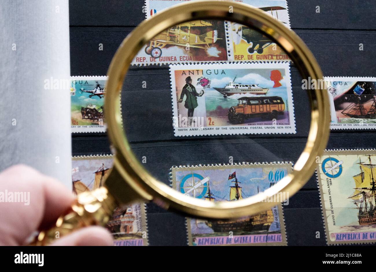 Mosca, Russia, Marzo 2022: Hobby - raccolta di francobolli. Guardando un timbro postale di 2 cent di Antigua con motoscafo e autobus retrò attraverso un magnif dorato Foto Stock