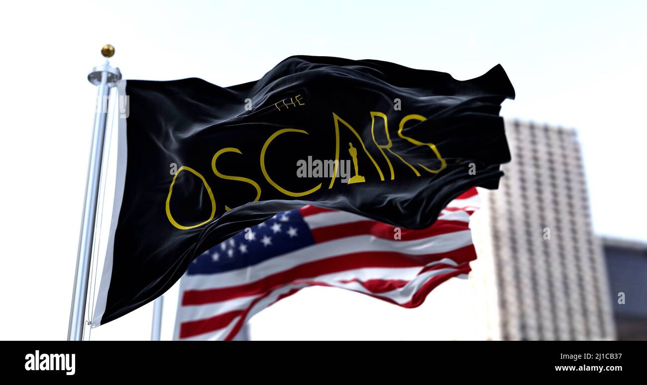Hollywood, CA, USA, marzo 2022: La bandiera con il logo Academy Awards ondeggiante con la bandiera americana sfocata sullo sfondo. L'Academy Award, alias Foto Stock