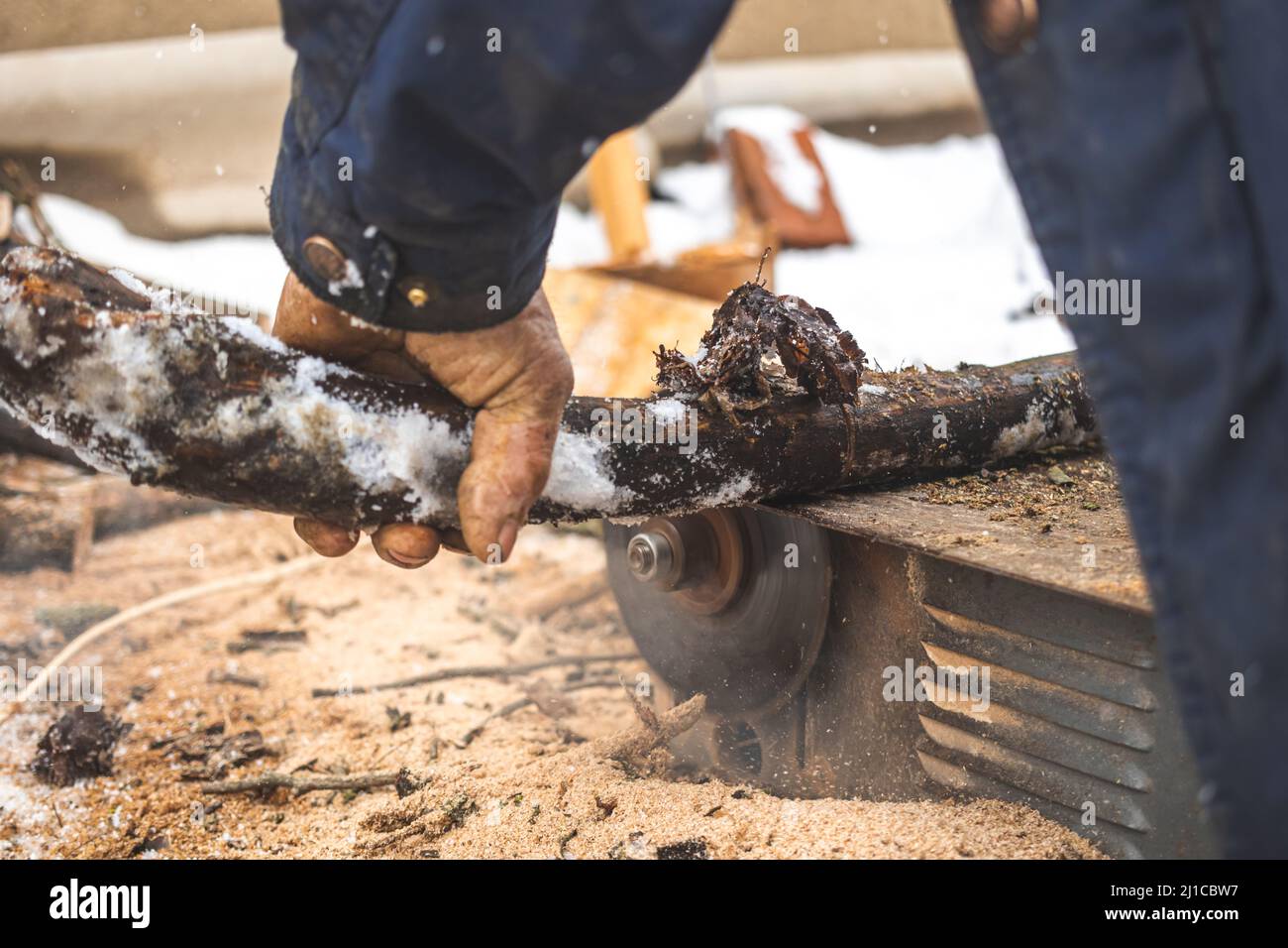 Uomo che taglia legno usando sega circolare stazionaria all'aperto in inverno per il primo piano di accensione Foto Stock