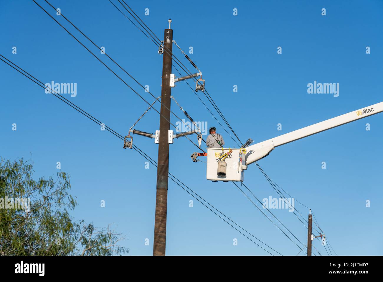 Un operatore di costruzioni elettriche o un lineman che lavora in una benna rialzata per eseguire nuove linee di trasmissione elettrica. Foto Stock