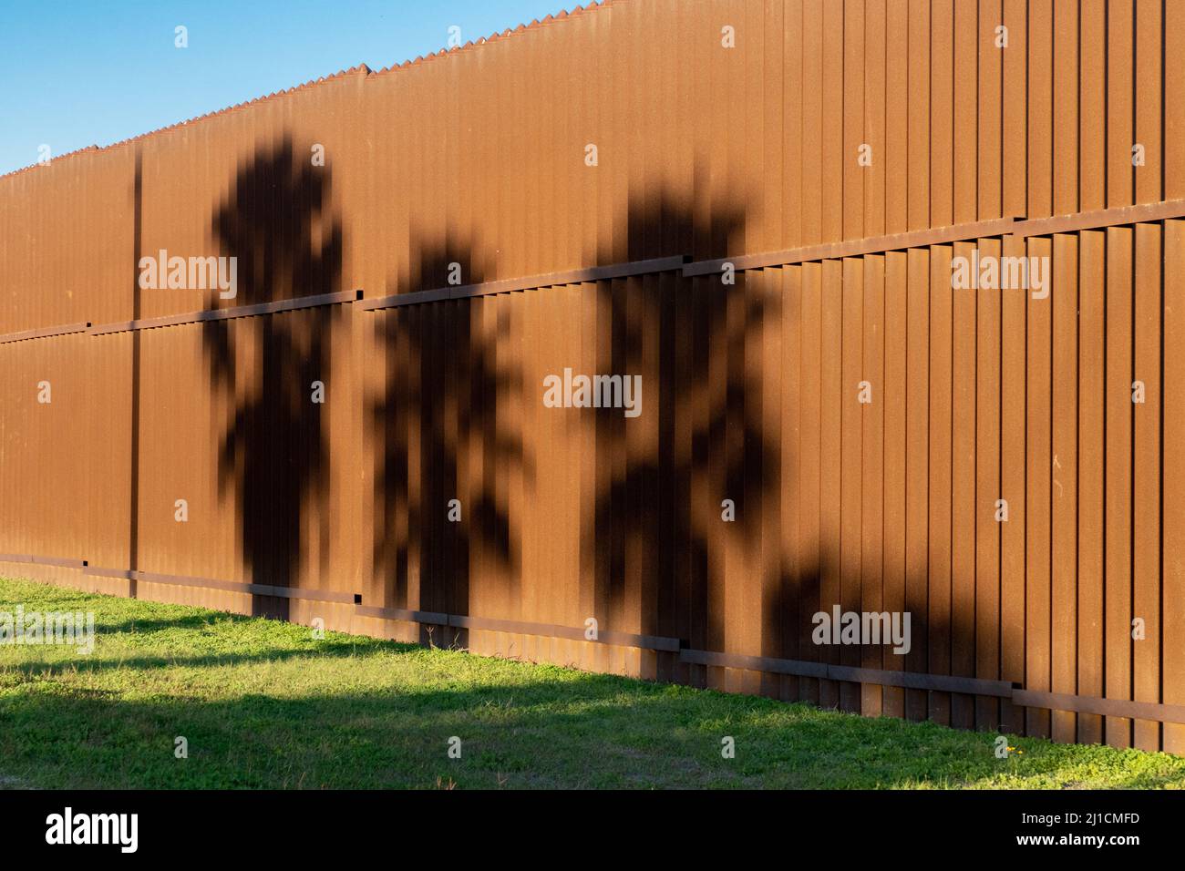 Ombre di palme sul muro di confine tra Stati Uniti e Messico vicino a Brownsville, Texas alla luce del tardo pomeriggio. Vista dal lato del Texas della parete. Foto Stock