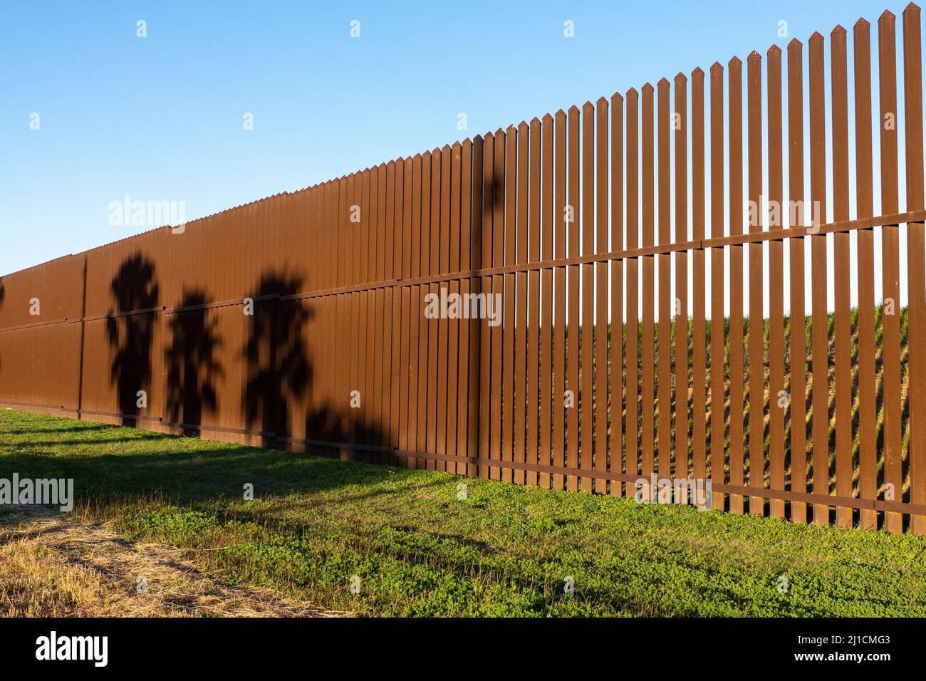 Ombre di palme sul muro di confine tra Stati Uniti e Messico vicino a Brownsville, Texas alla luce del tardo pomeriggio. Vista dal lato del Texas della parete. Foto Stock